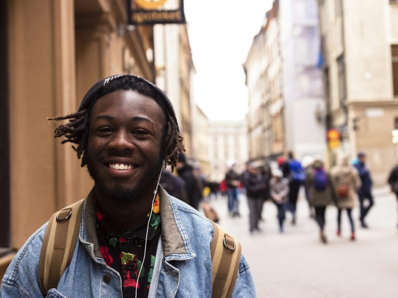 A smiling student with a backpack on a busy street