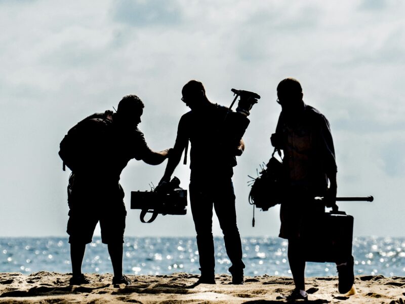 Silhouettes of a film crew with camera gear on the beach