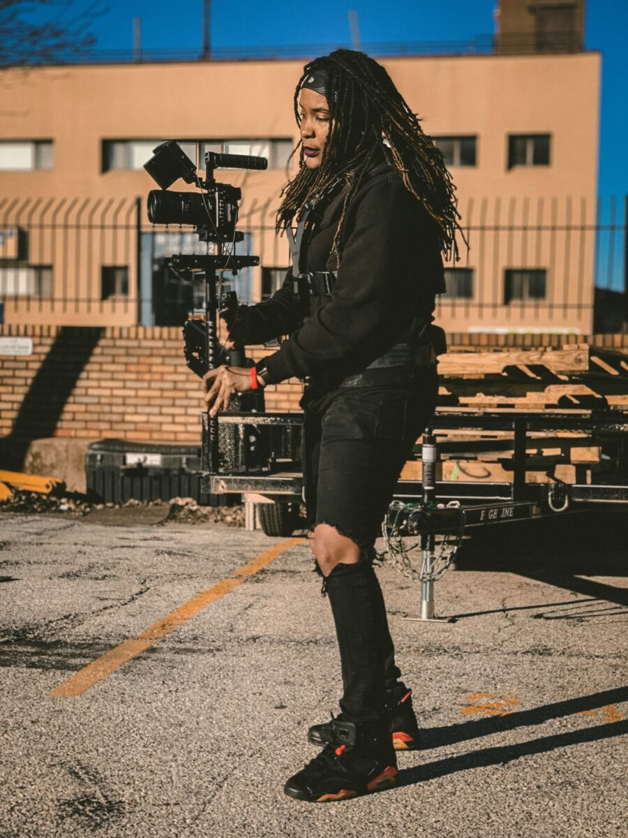 A young Black filmmaker walking with a camera rig on a city rooftop