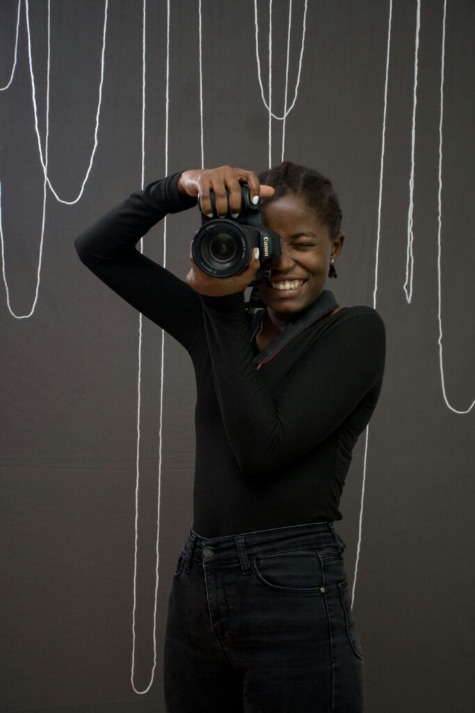 A young Black woman smiling behind a camera