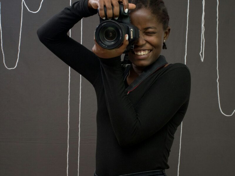 A young Black woman smiling behind a camera